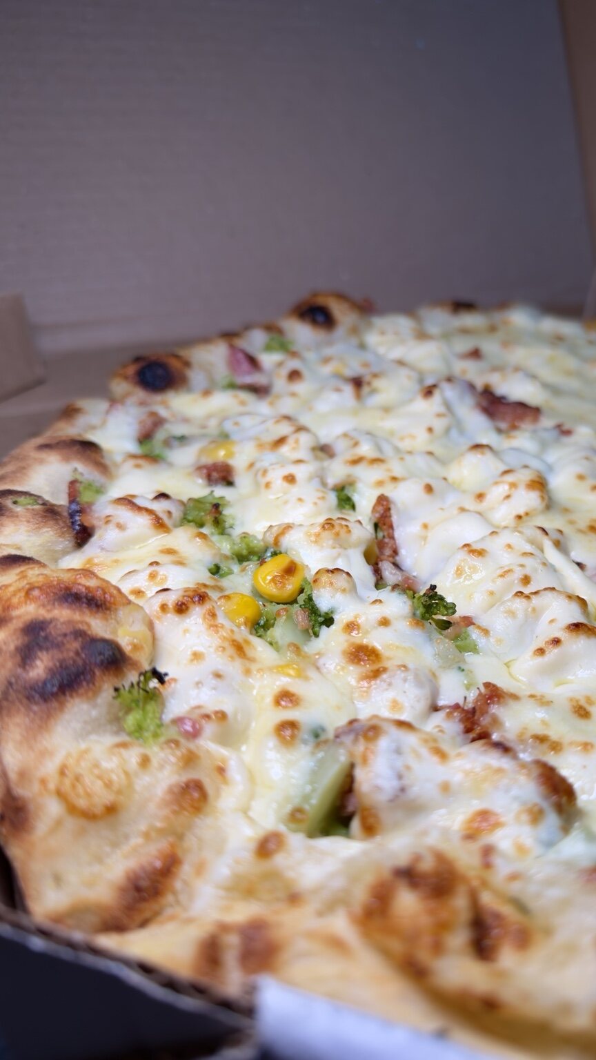 Close de uma pizza da Luigi’s com queijo gratinado, brócolis, milho e bacon